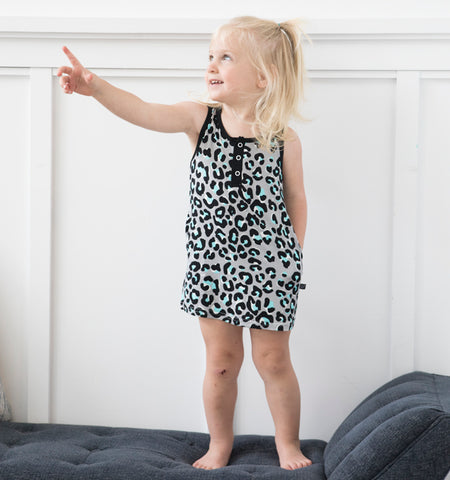 A girl is standing on a bench pointing off camera while wearing a leopard print tank dress. Her other hand is in her pocket! 