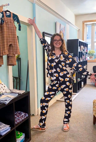 A young woman strikes a pose in a store after trying on new pajamas. The pjs are black with fried eggs all over them! 