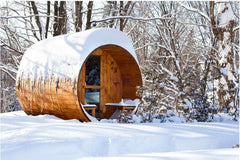 Snow covered barrel sauna with porch outside during a winter day