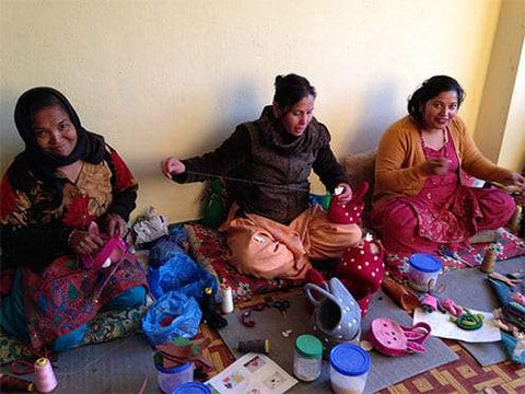 Three makers from Pashom, making felt toys. The makers on the left and right are smiling and the maker in the middle is looking down at the toy she is making.