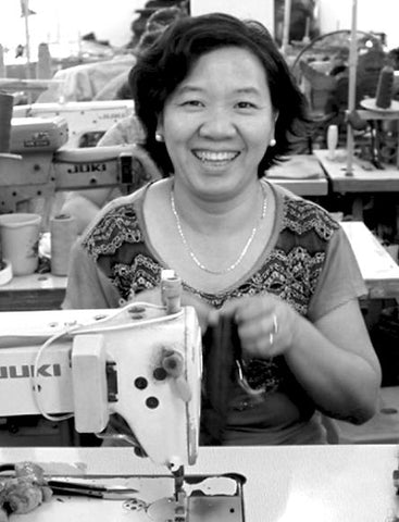 One of Just Trade's Fair Trader artisans in Vietnam sits behind a sewing machine, smiling at the camera.