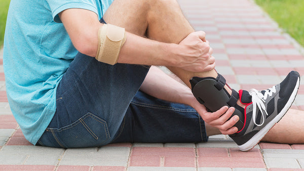 A man sitting on the ground holding his leg, wearing an ankle brace