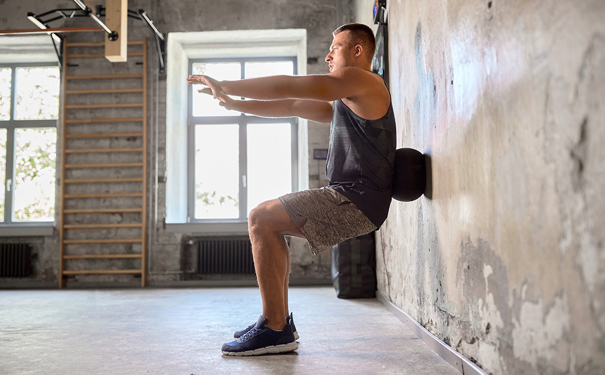 A man in a gym does wall squats with a foam roller to improve balance.