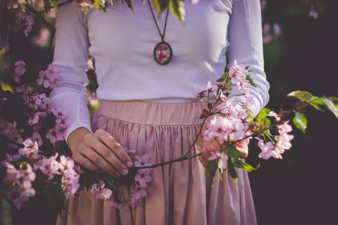 Image of a woman who is holding some cherry blossoms and has a floral urn necklace she is wearing.