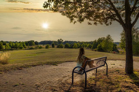 Woman sitting at a bench near a tree where a loved one's ashes have been buried