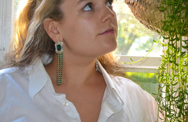 Alexis in the emerald Maude Crystal Drop Earrings, next to a plant