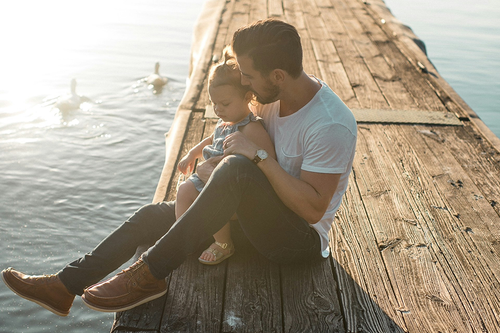 father and daughter sat on a pier looking into the water