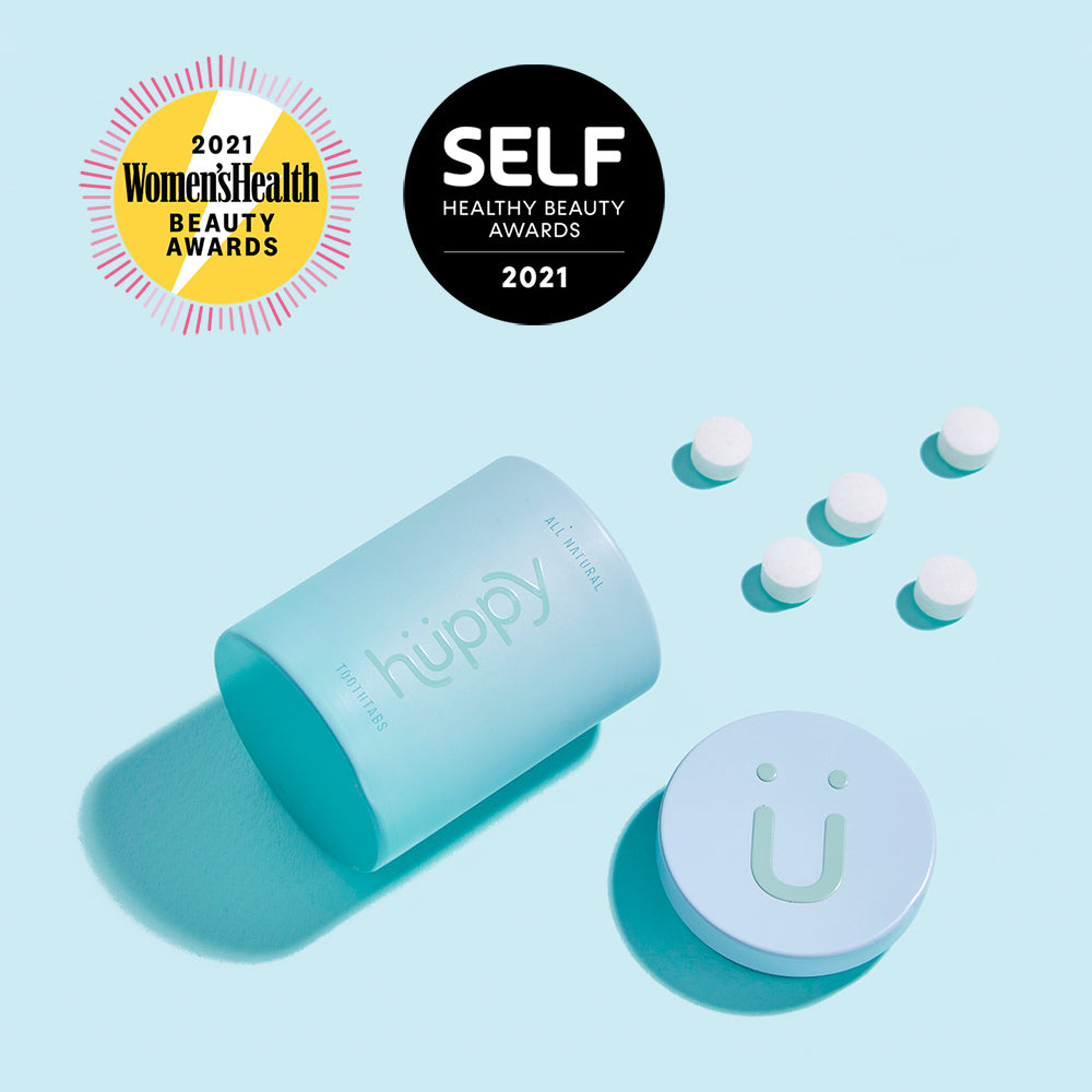 Blue huppy aluminum cup open with toothpaste tablets outside it. Awards labels at the top readh: 2021 Womens Health Beauty Awards and SELF Healthy Beauty Awards 2021.