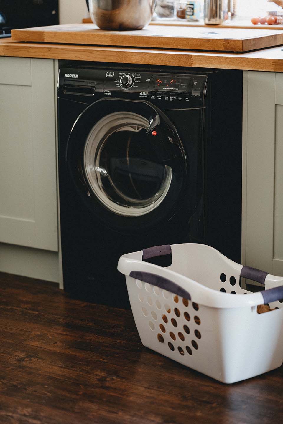 black hoover front loading washing machine with A+++ rating. White laundry basket in front of washer.