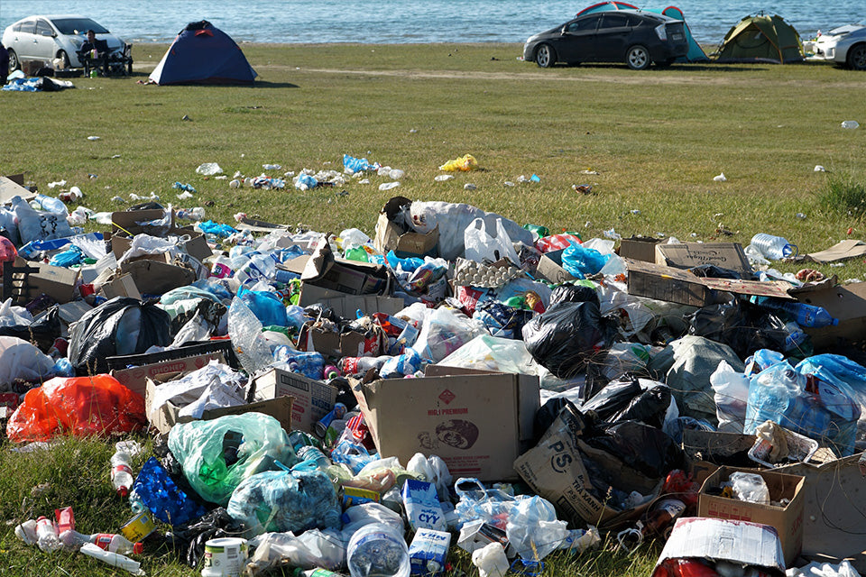 cars leaving a camp site by the beach with piles of plastic and trash accumulated around no trash cans