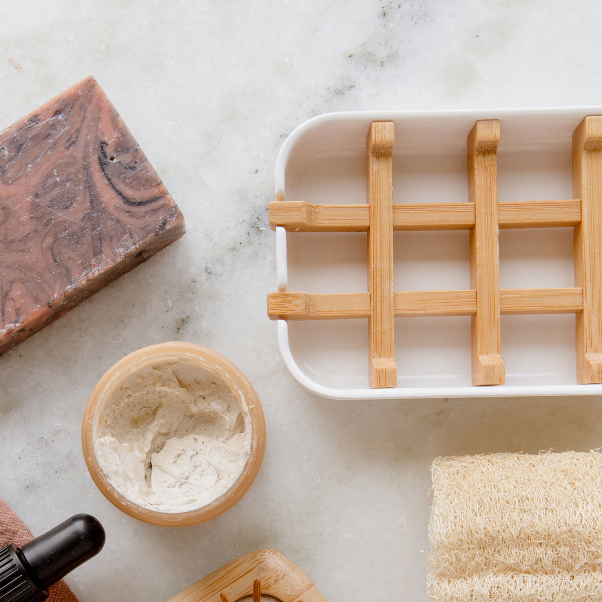 cornstarch soap dishes with bamboo slats in white next to a soap bar, open container of skin product, and loofah