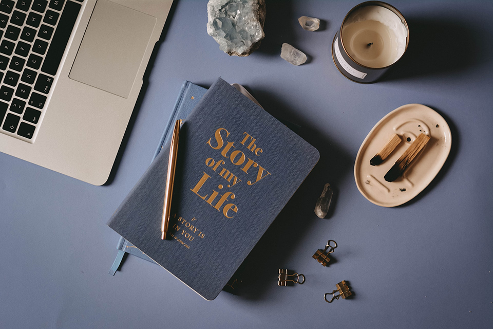 A navy blue journal next to an open laptop, some gem stones, and incense