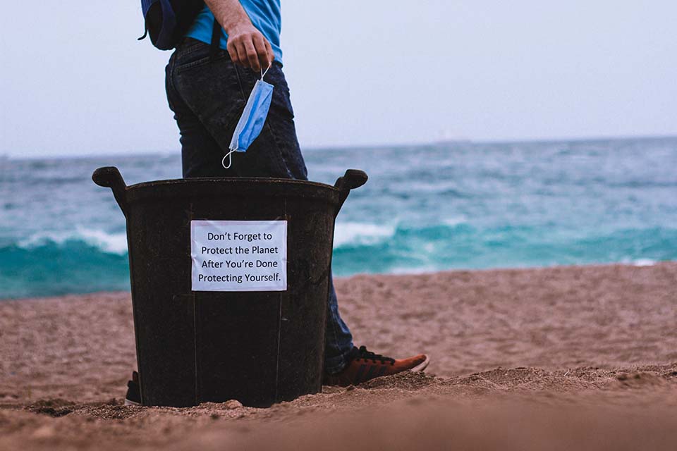 Person holding a mask standing next to a black tote bag that reads 