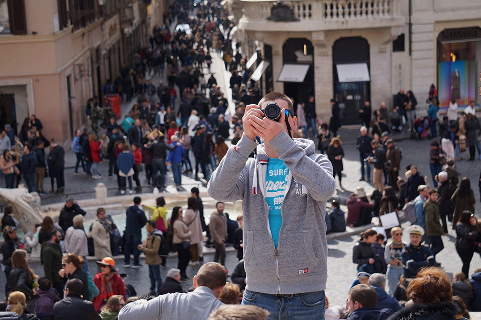 a person standing to take a photograph in a crowded city center.