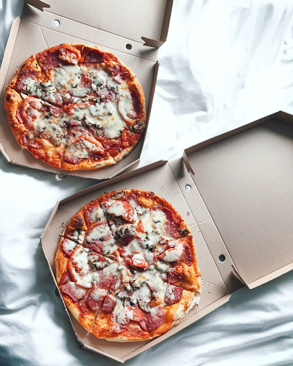 two whole pizzas inside cardboard pizza boxes.