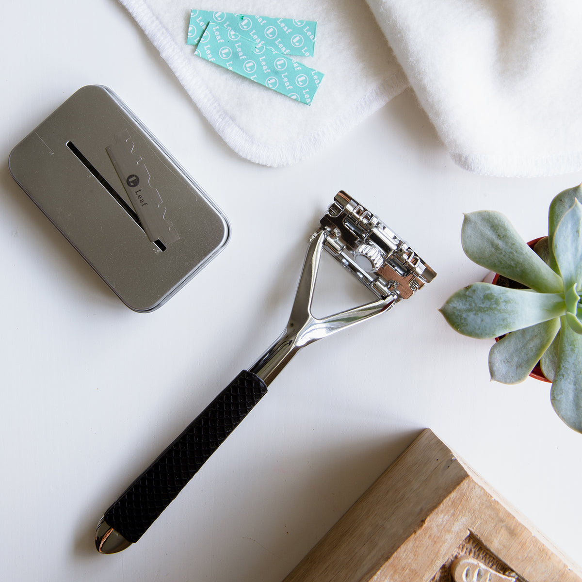 leaf razor in stainless steel with black silicone handle. sitting next to blade recycling tin.