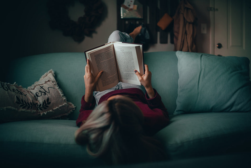 woman lying upside down, reading a book on a turquoise sofa