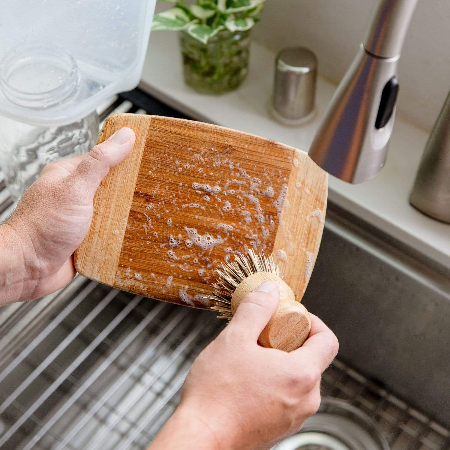 Hands using Pot Scrubber to wash a small bamboo cutting board over a stainless steel sink