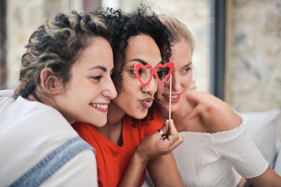 three women posing for a photo with woman in the center holding up cutout heart glasses