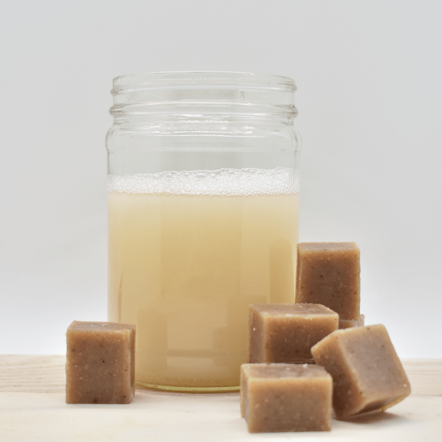 5 small brown cubes surround a mason jar almost full of light brown liquid (dissolved soap).