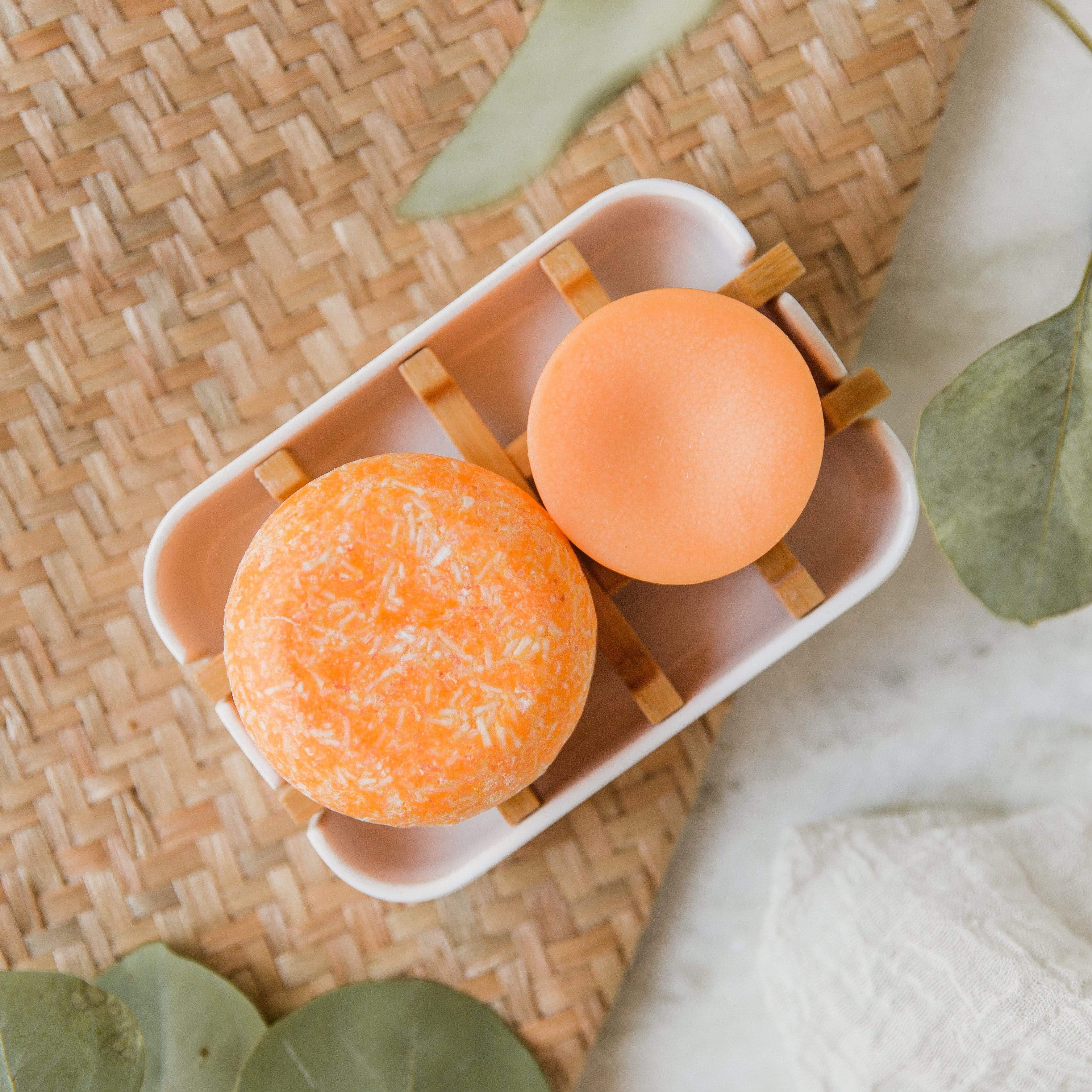 Orange shampoo & conditioner bar on soap dish with wood soap saver underneath