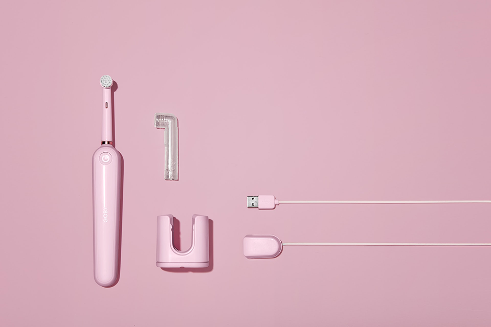 Pink electric toothbrush with all it's attachments and various plastic parts: stand, head cover, usb port and cord