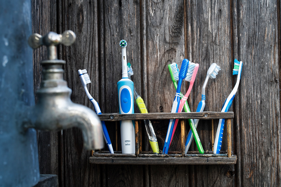 wooden shelf attached to wooden wall containing quite a few varieties of in use toothbrushes