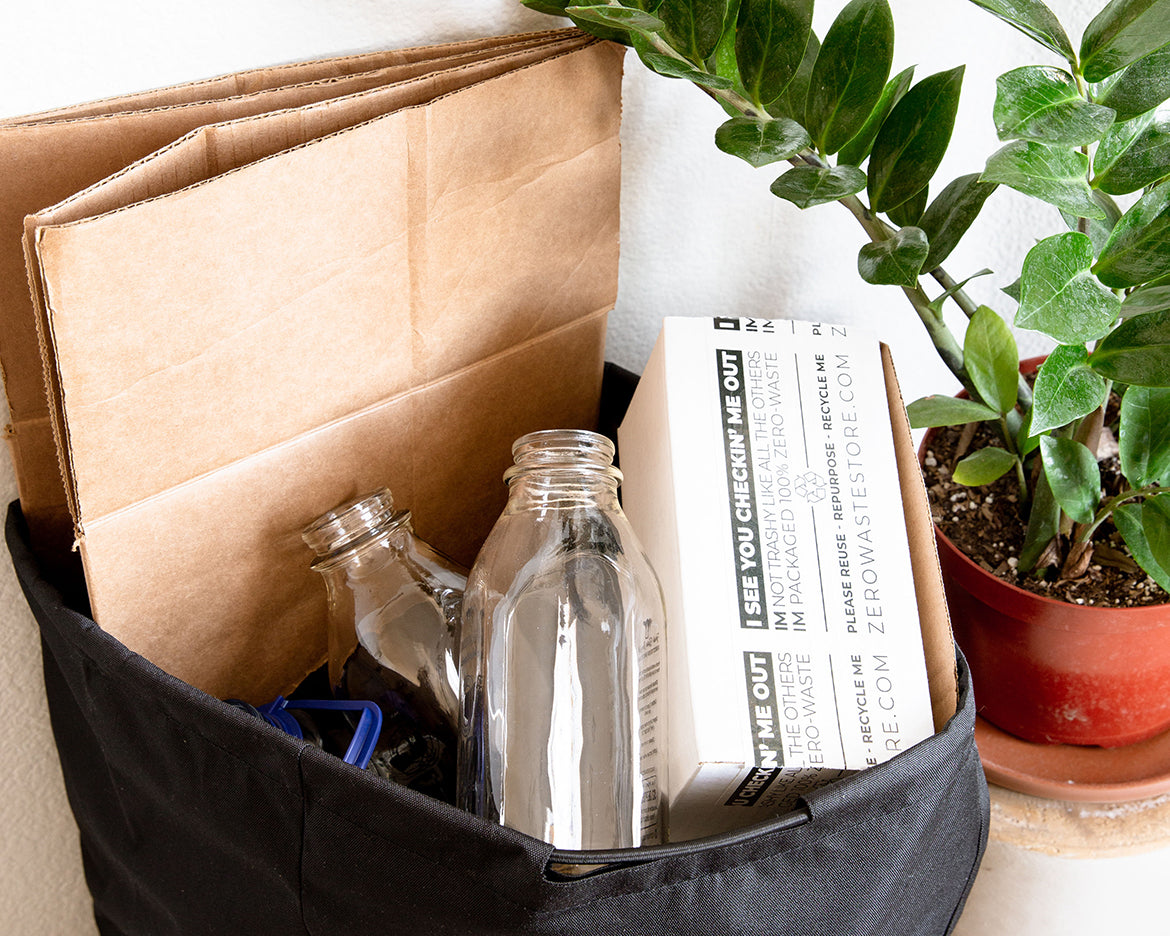 A reusable recycling bag filled with cardboard, two glass bottles, and a Zero Waste Store taped packaging box