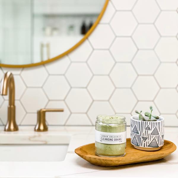 glass jar sitting on wood plate in a bathroom. Contents inside jar are a pea green, jar has a white illegible label.