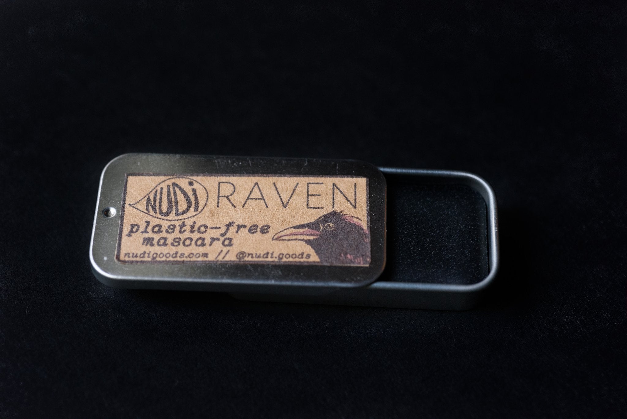 Black solid mascara inside metal tin. Lid of tin reads: Nudi Raven plastic-free mascara