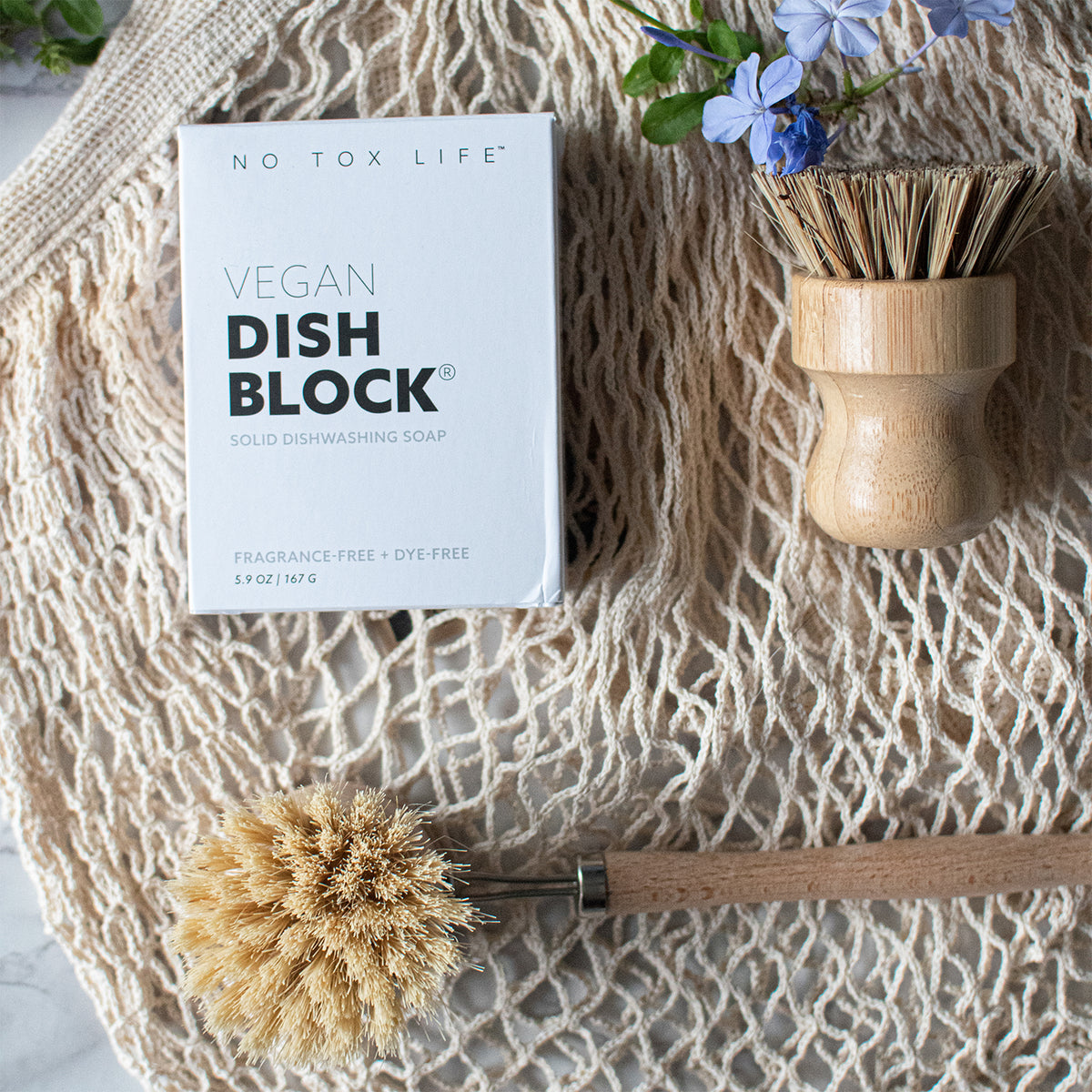 vegan dish block box, next to pot scrubber, above dish brush sitting on a mesh produce bag