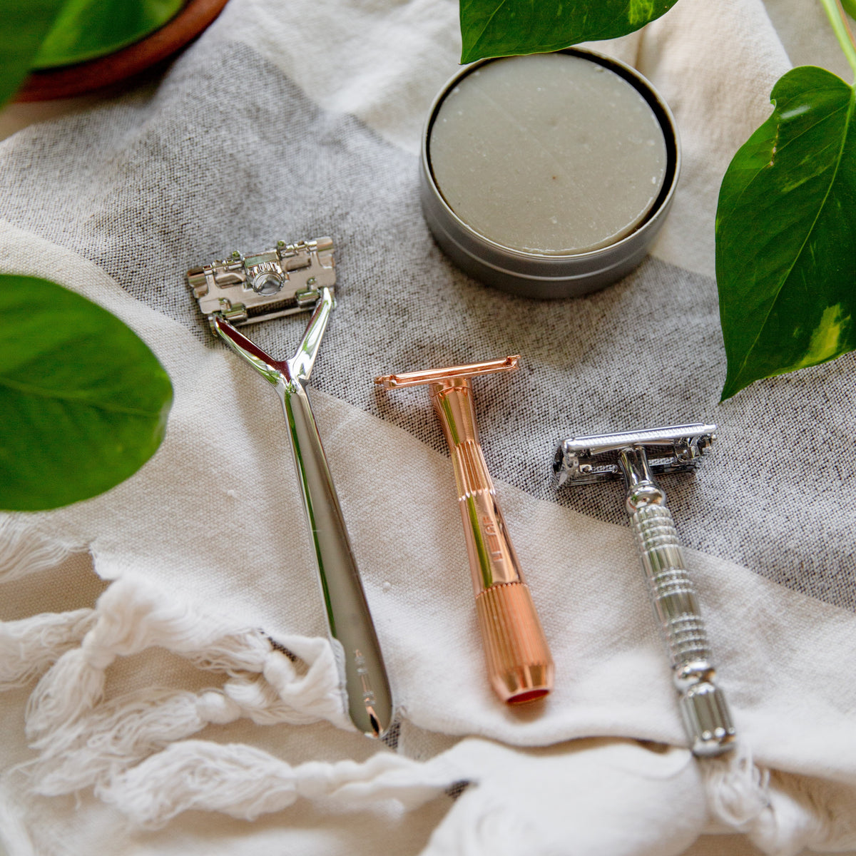 Three different safety razors and a tin of shaving balm on a striped linen