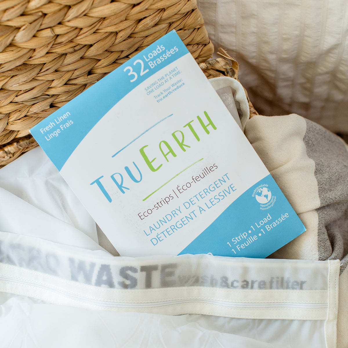 1 cardboard package of TruEarth eco-strips sitting in a laundry basket of white clothes. Box reads 32 loads TruEarth eco-strips laundry detergent