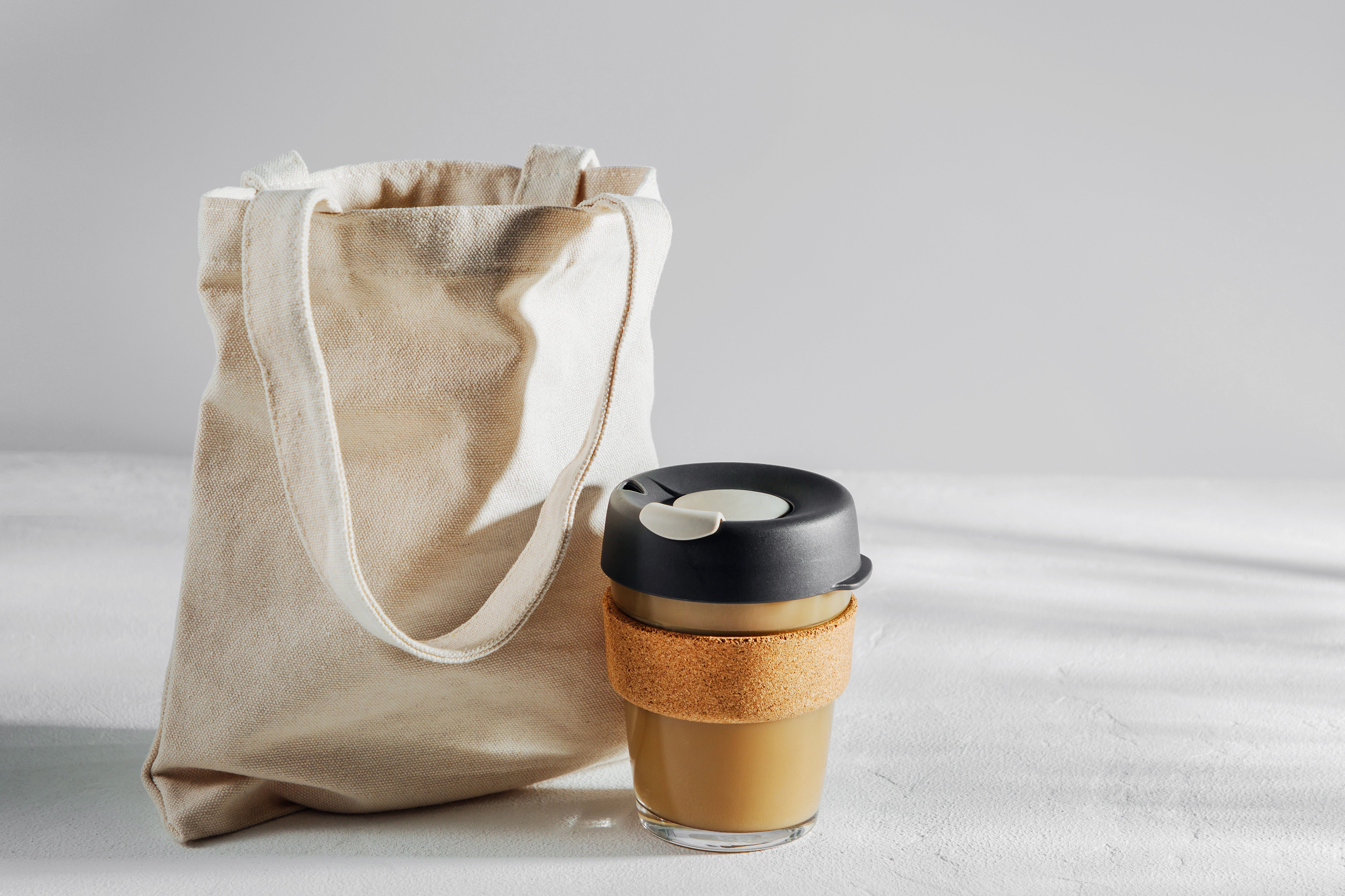 reusable canvas bag and glass coffee tumbler against a white background