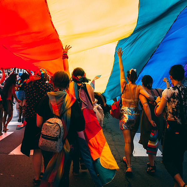 A group of young people under a large rainbow flag during Pride