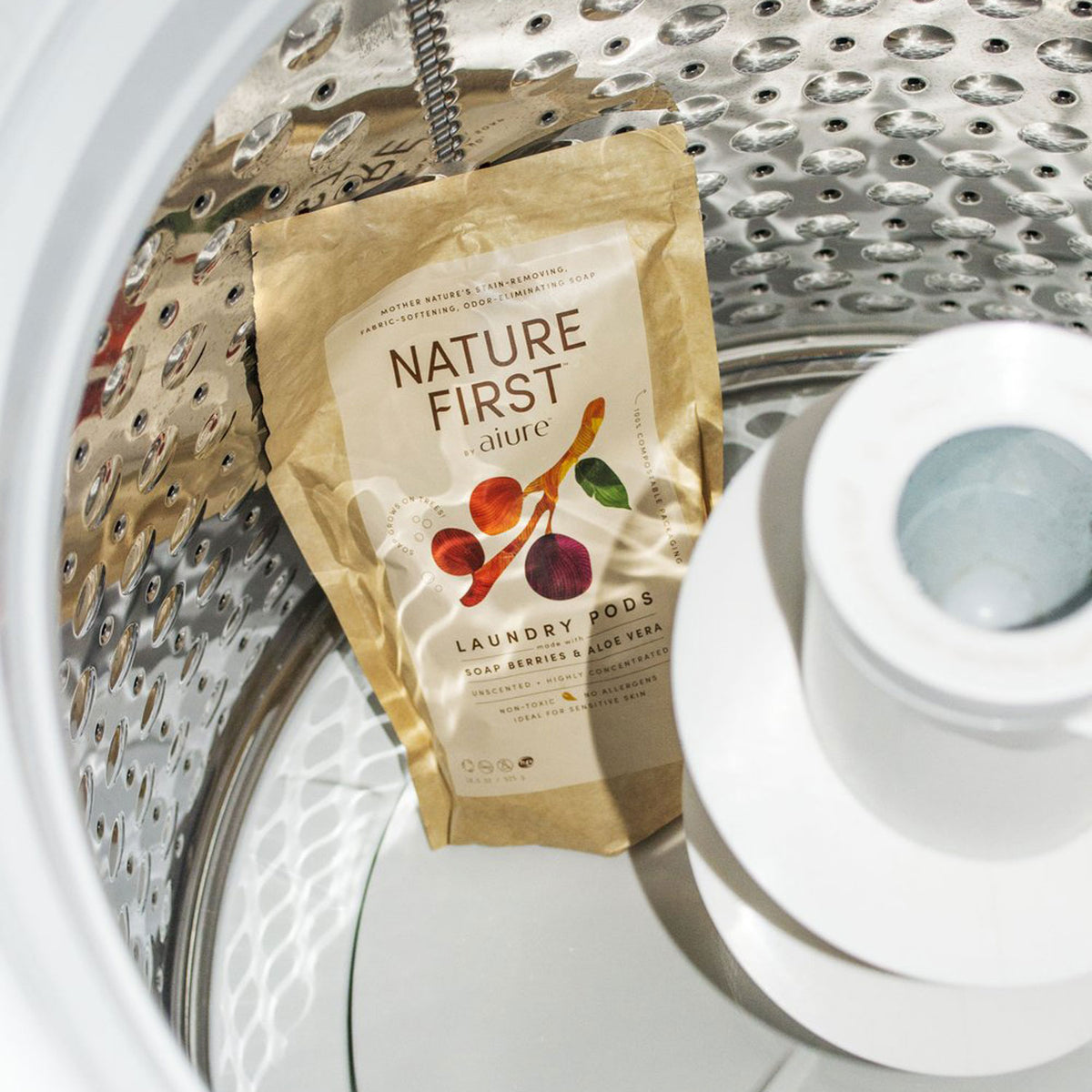 A bag of detergent pods sitting in an empty washing machine. Bag reads Nature First - aiure Laundry Pods