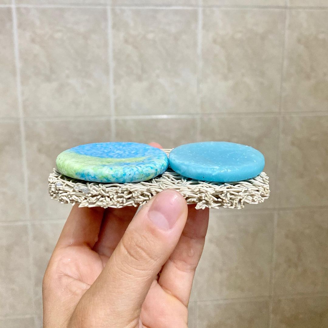 a hand holding a soap lift containing two used blue shampoo and conditioner bars