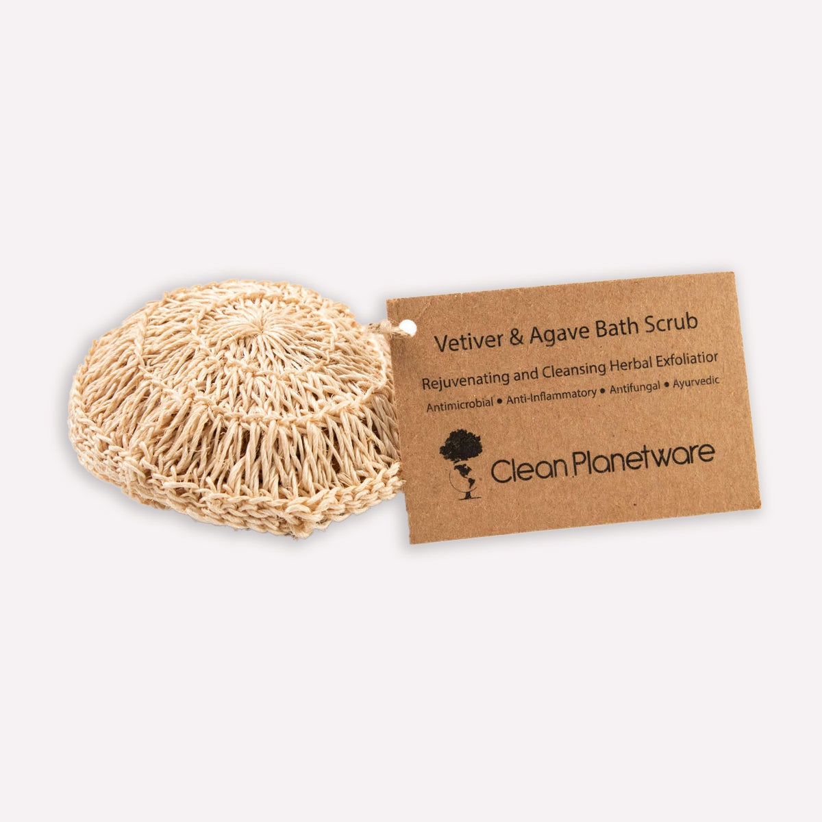 : Circular natural bath scrub with cardboard tag that reads: Vetiver & Agave Bath Scrub Rejuvenating and Cleansing Herbal Exfoliator. Clean Planetware