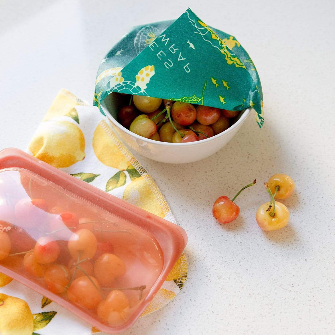 A bowl of cherries partially covered by a teal beeswax wrap in ocean print