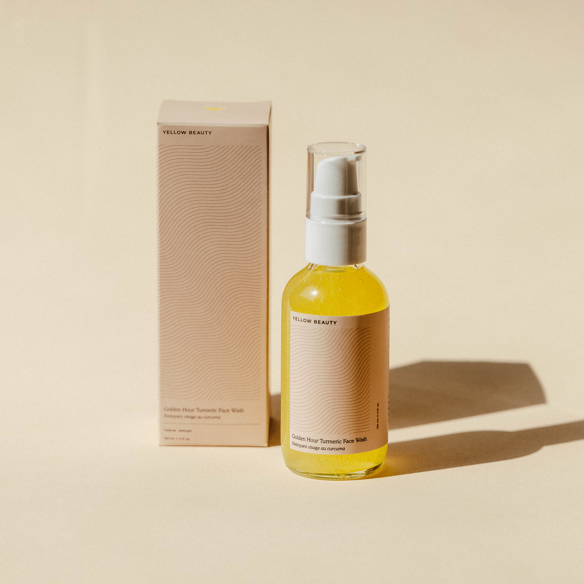 Glass jar with brown plain label and white pump next to cardboard box. Face wash inside bottle is a light golden/yellow color