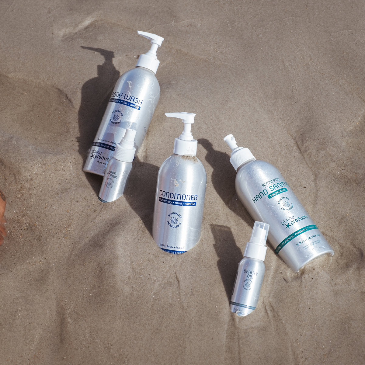 Metal bottles of hair and body care products partially buried in sand