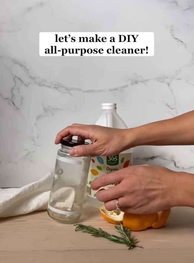video screenshot of making a diy cleaner. Empty glass jar, white vinegar bottle, orange peels, and rosemary herbs are shown.