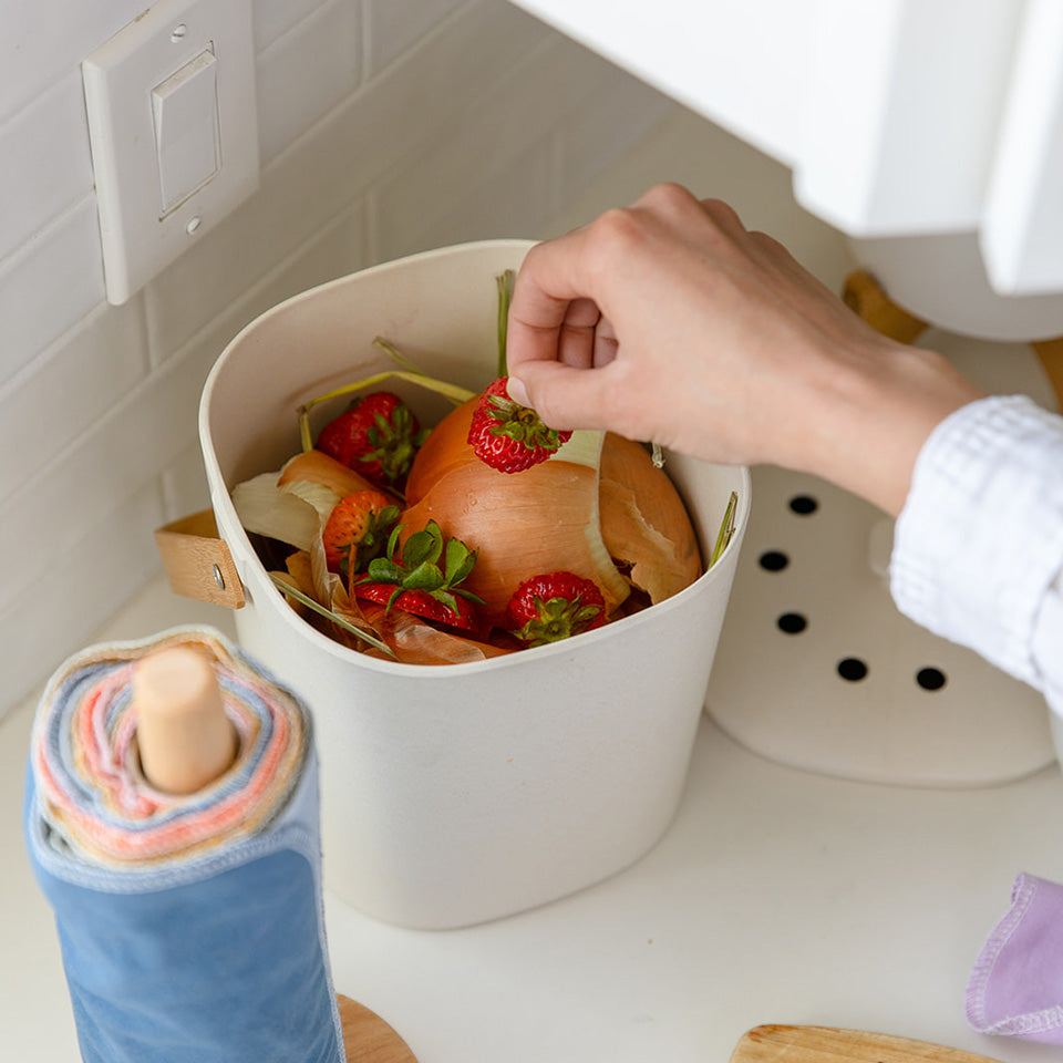 Hand placing strawberry tops in a white compost bin