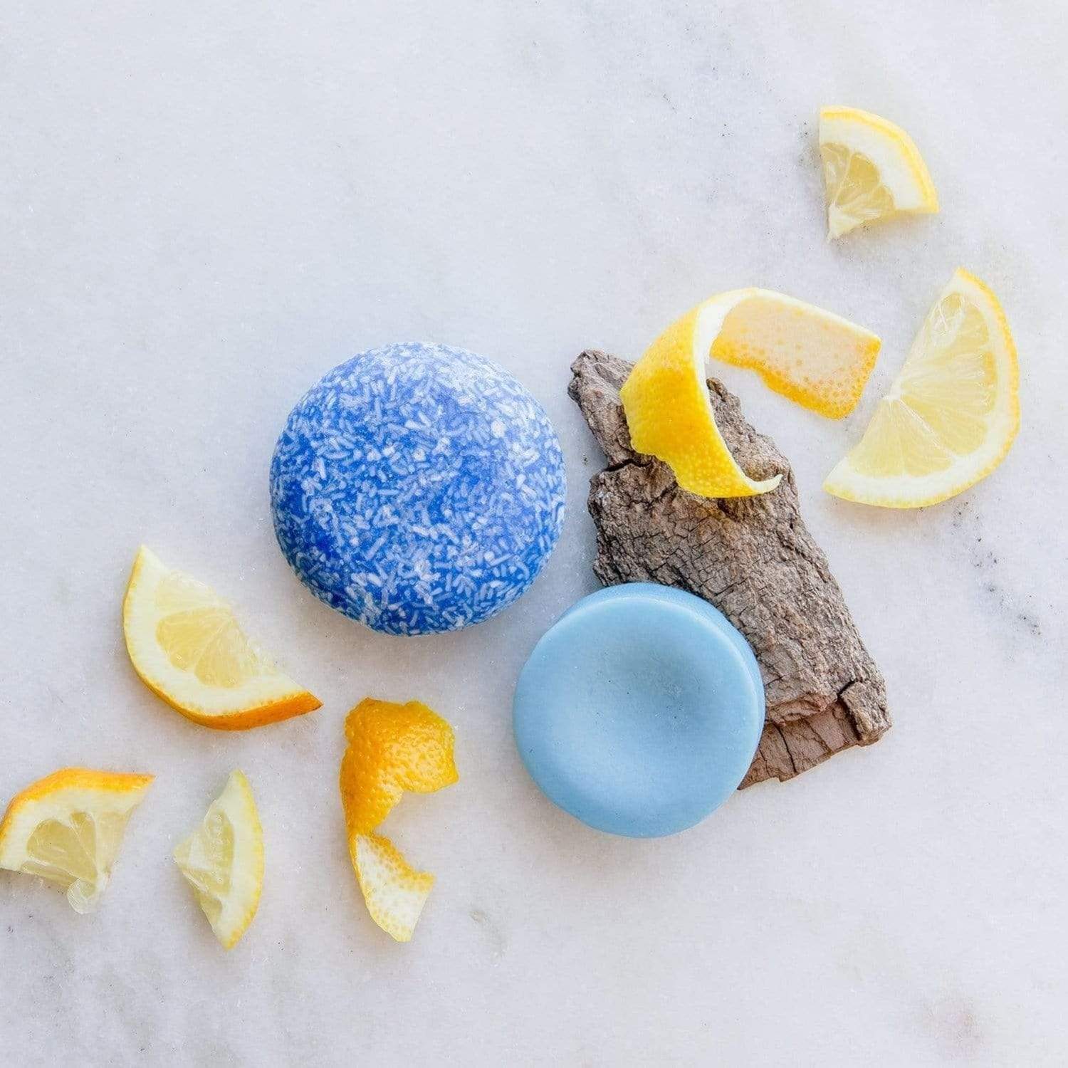 (blue) cobalt shampoo and conditioner bars from suds & co resting on bark surrounding by lemon peels