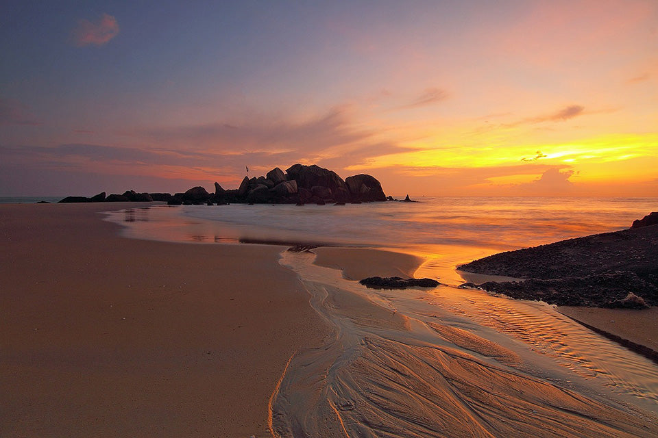 A beautiful, clean, pristine beach at sunrise with a pile of rocks in the near distance. What we want all beaches to look like (free of plastic)