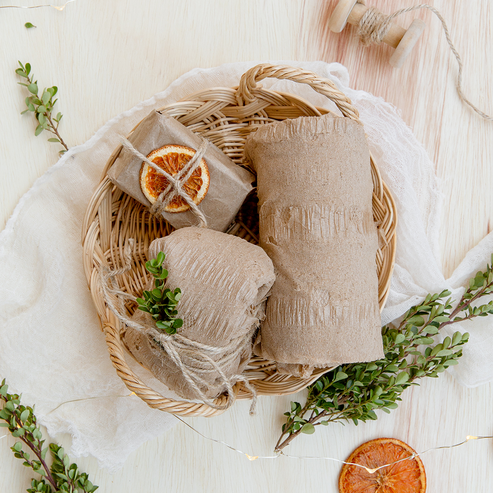3 gifts wrapped in recycled kraft paper, tied with twine, adorned with leaf sprigs and dried orange slices