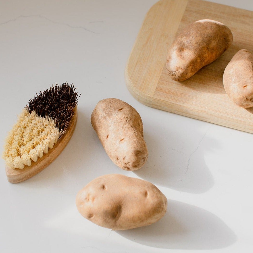 Two-toned vegetable brush next to a cutting board with potatoes.