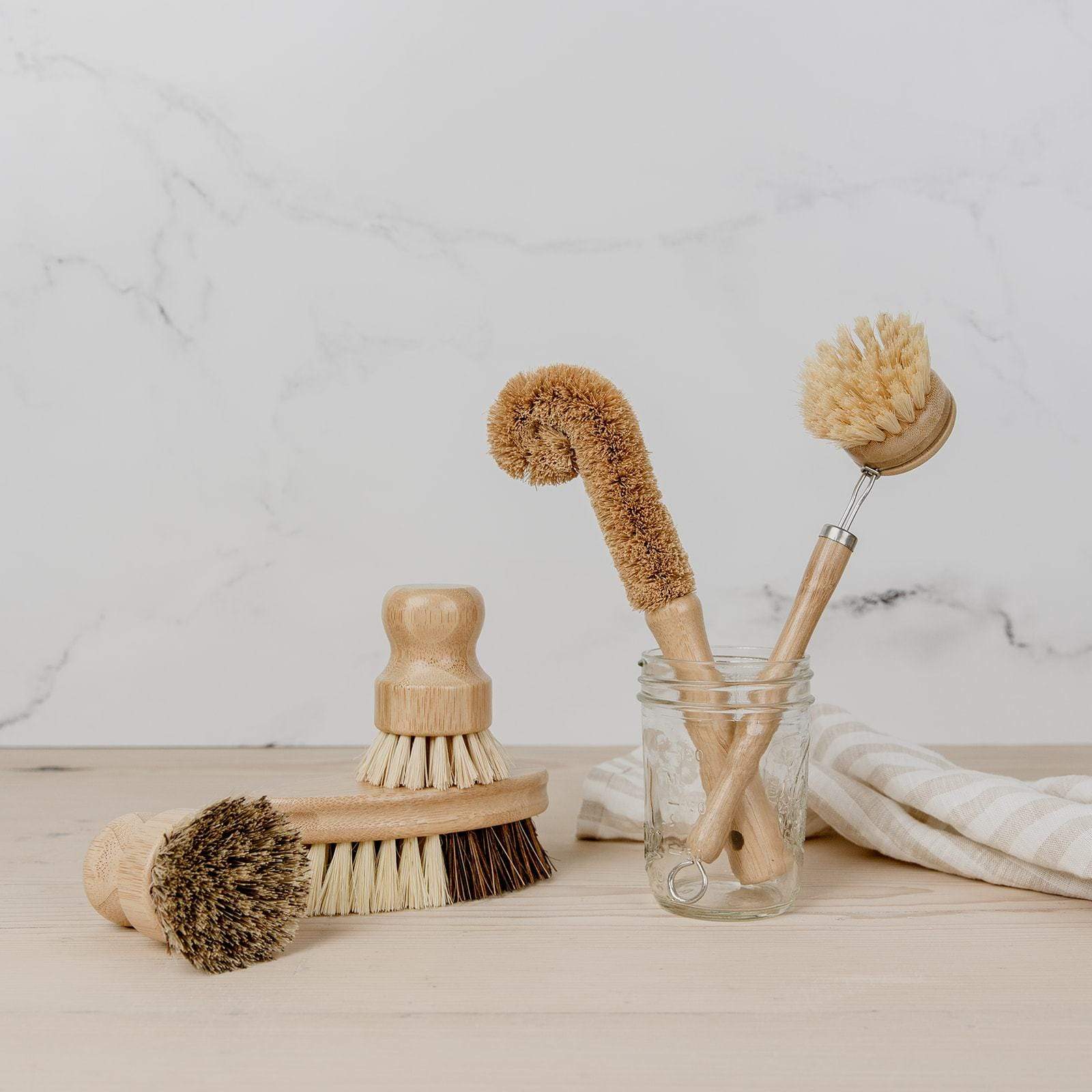 all 5 brushes from the zero waste dish brush kit on a countertop. Bottle brush and long handled brush are in a glass jar, the others are on the counter.