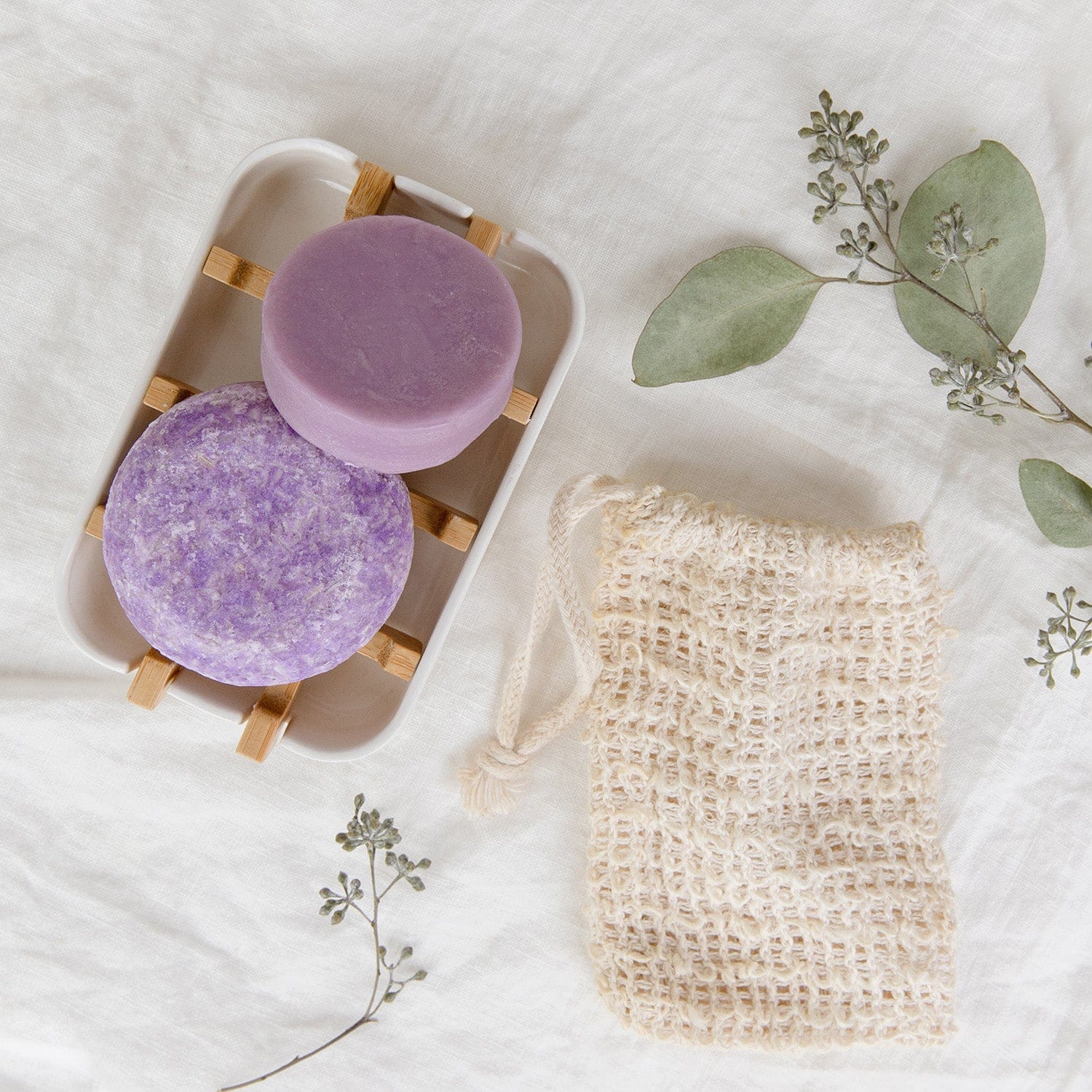 (blue and purple) oasis shampoo and conditioner bars from suds & co on a soap list near a bathtub ledge.