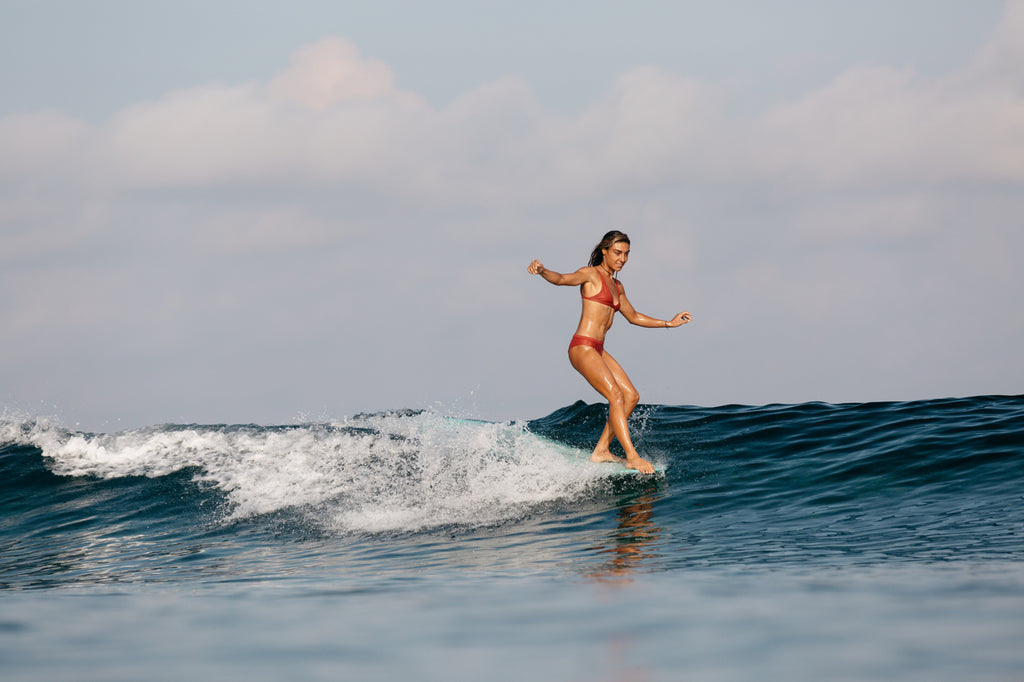 Woman doing a cheater five on a surfboard wearing a surf bikini in burnt sienna
